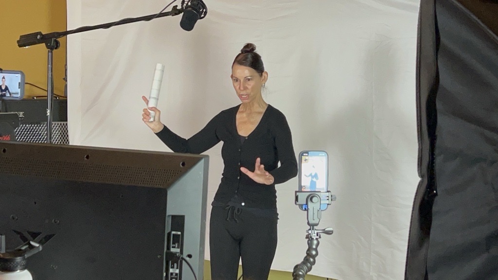 A performer works to camera on a TW3 shoot, boom mic, monitor and lighting rigged around her.