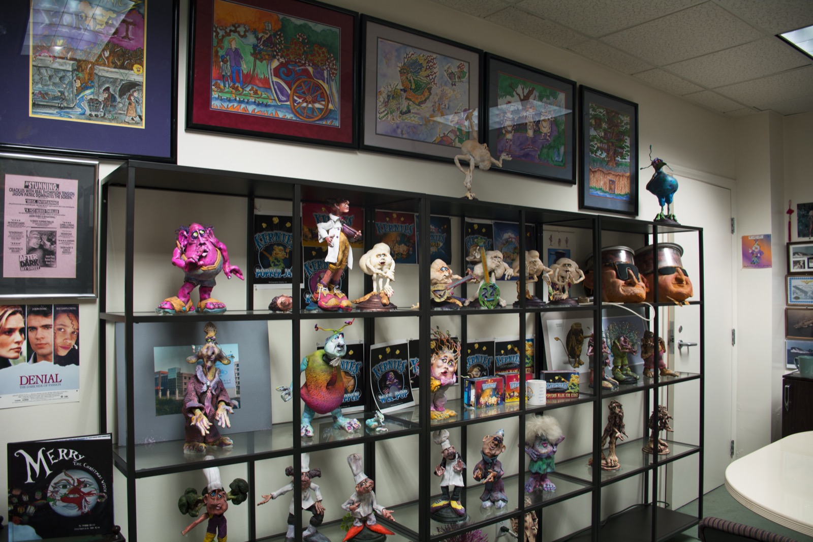 Shelves of original TW3 character maquettes — creatures, fish-folk and goblins in bright sculpted color, under walls of framed character art.