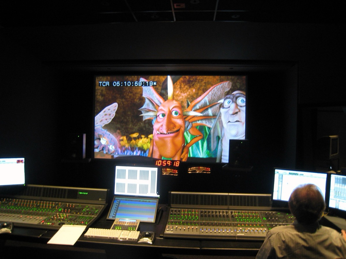 A dub stage: a mixing console and timecode display facing a screen of animated Dwegons mid-scene, the engineer at the desk.