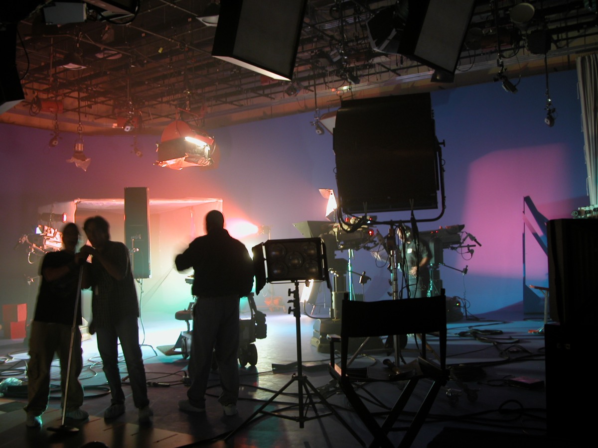 Crew work in silhouette on a darkened stage washed in pink and green light, lighting instruments rigged overhead.