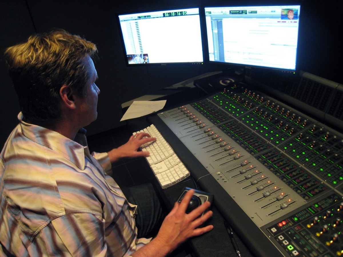 An engineer works a large mixing console under a bank of monitors.