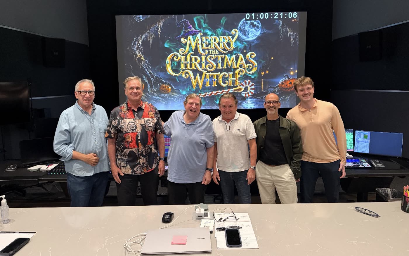 The finishing team on the dub stage, the Merry The Christmas Witch title card on the screen behind them with timecode running.