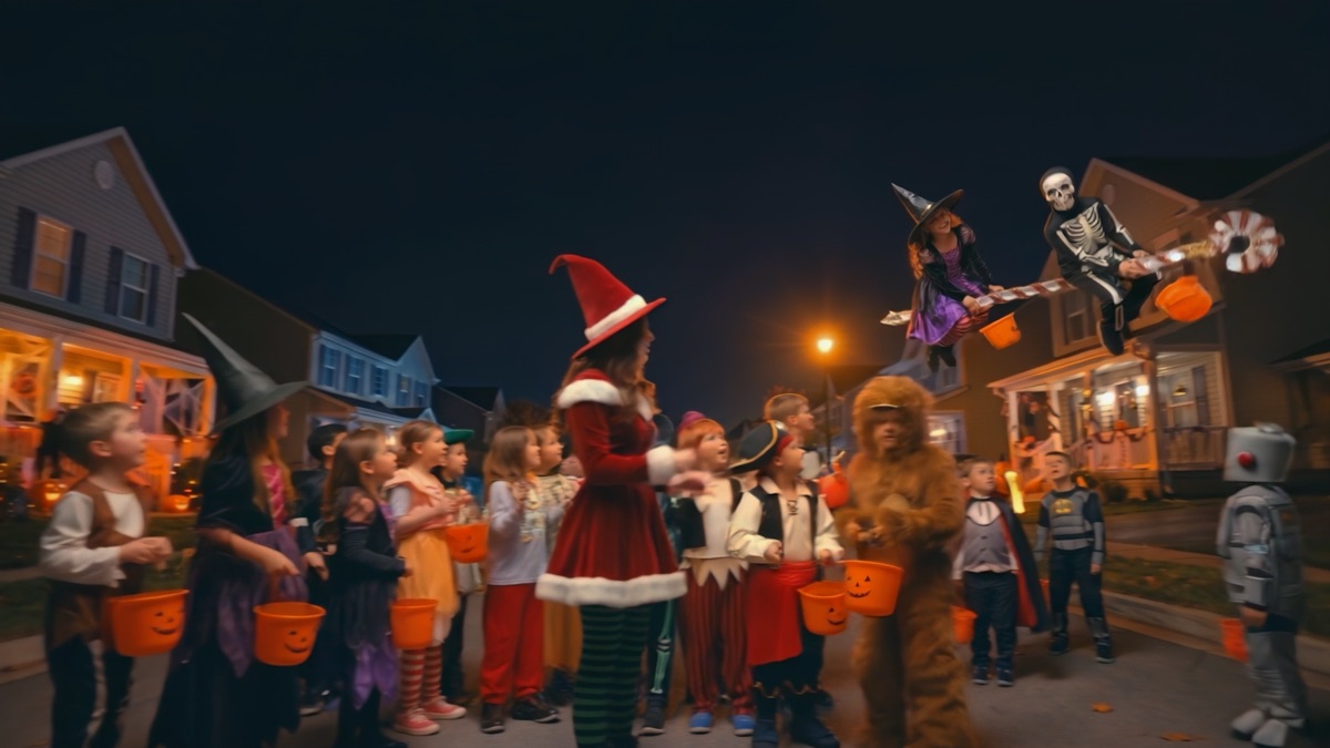 A costumed crowd fills a village street at night for a Halloween parade.