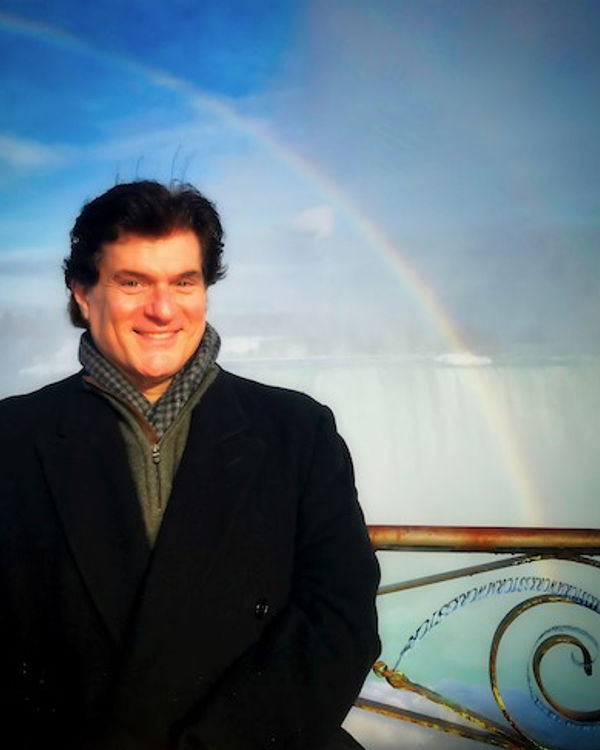 Stephen Melillo, standing before Niagara Falls with a rainbow behind him.