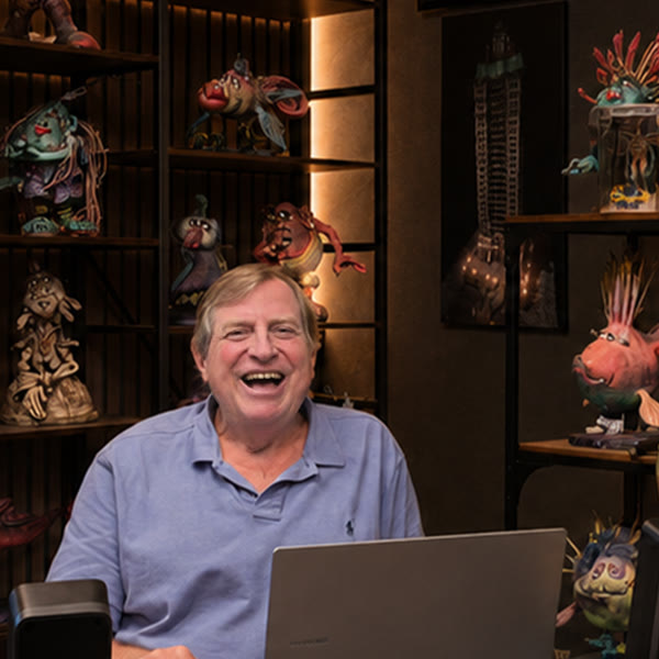 Tom Walsh at his desk, laughing, surrounded by shelves of original TW3 character maquettes.